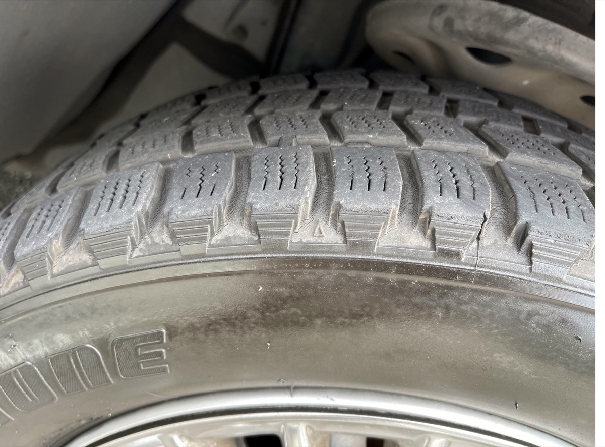 Close-up of a tire groove showing a molded wear bar and a raised tread wear indicator block.